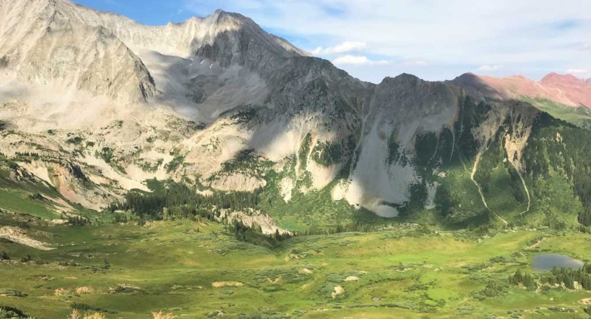 A green valley lies below a rocky mountain 